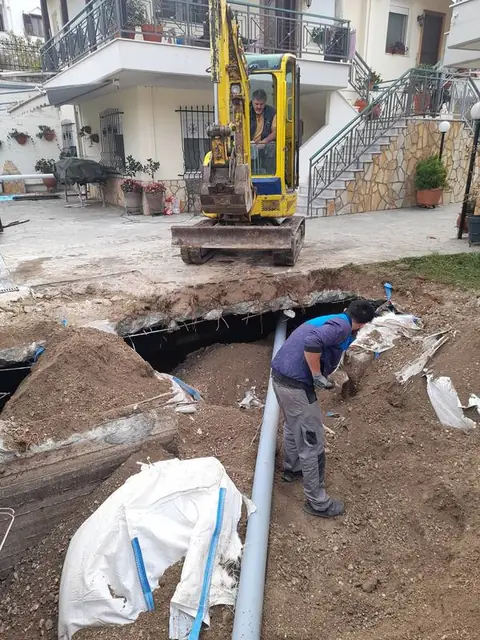 Εκσκαφέας και τεχνικός σε εργασία κατασκευής δικτύου αποχέτευσης σε αυλή κατοικίας